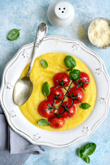 Traditional italian dish polenta with parmesan cheese and grilled tomato.