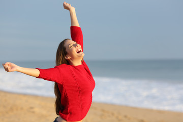 Excited girl in red on a beach raising arms