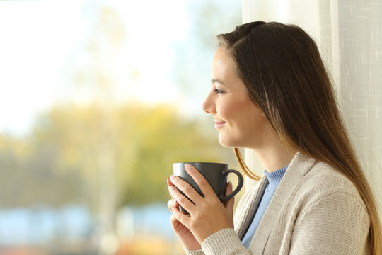 Relaxed lady holding coffee cup looks outside at home