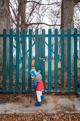Kind steht vor geschlossenem Gartentor. Kid standing in front of closed garden gate.