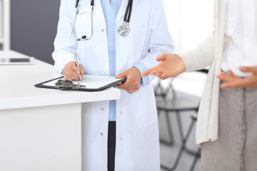 Unknown doctor and  female patient  discussing something while standing near reception desk in emergency hospital. Physician at work in clinic. Medicine and health care concept