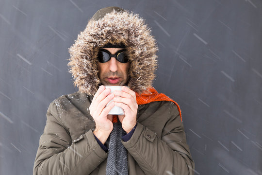 Portrait of a single male winter adventurer wearing a warm green coat with fur hood, an orange scarf and black retro style goggles drinking from a metal cup