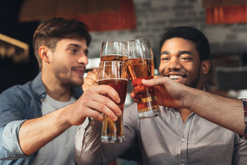 Male friends drinking beer and clinking glasses at bar