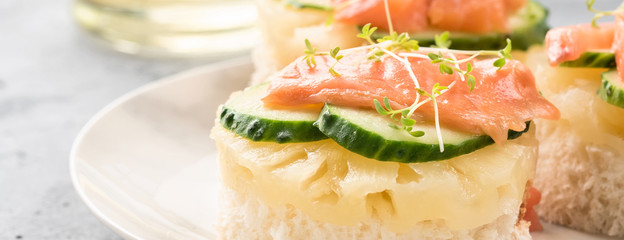 Bruschetta toast of white bread with slices of pineapple cucumber fish salmon and fresh green sprouts. Served on a white plate on table with mineral water olive oil