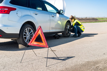 Woman driver changing damaged wheel on roadside