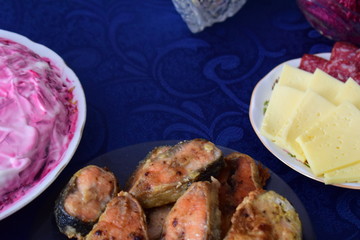 Festive snacks and salad on the table. Fried red fish. Sliced sausage and cheese. Salad herring under fur coat. Russian traditional cuisine.