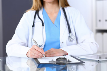 Female doctor filling up medical form on a clipboard, closeup. Healthcare, insurance and medicine concept