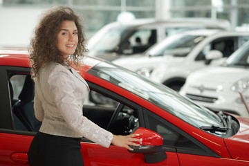 Gorgeous woman posing near red car in car center.