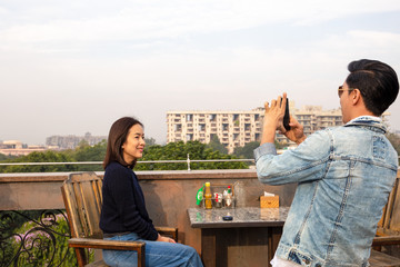 Couple using cell phone taking pictures of each other at cafe outdoor.