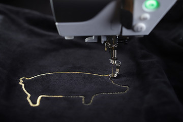 Tilted front view on embroidery machine stitching pig motive with gold yarn on black velvetely fabric - foreground and background blanked out blurry