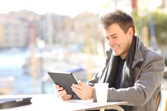Happy man using a tablet in a coffee shop of a port