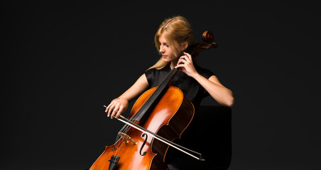 Young girl playing the cello on isolated black background - obrazy, fototapety, plakaty