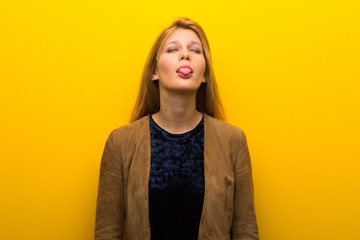 Blonde girl on vibrant yellow background showing tongue at the camera having funny look