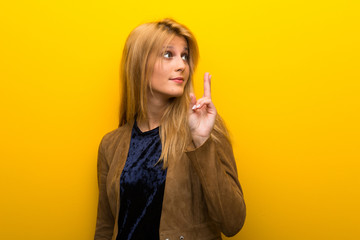 Blonde girl on vibrant yellow background with fingers crossing and wishing the best