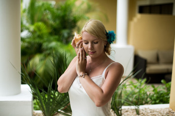 Young sexy woman in white pegnoir with seashell in her hands posing. Bride at the morning