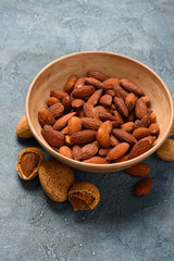 Fried salted almond nuts in a ceramic bowl on rustic background