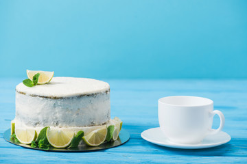 cake decorated with slices of lime near tea cup isolated on blue