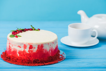 cake decorated with red currants and mint leaves near white cup and tea pot isolated on blue