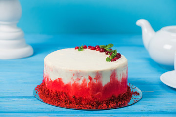 cake decorated with red currants and mint leaves between white cup, tea pot and stand isolated on blue