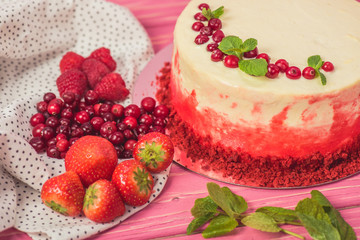 close up of white cake decorated with currants and mint leaves near fruits on pink surface
