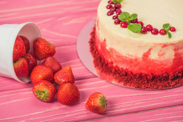 close up of white cake decorated with currants and mint leaves near fruits on pink wooden surface