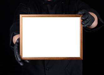 chef in black uniform and black latex gloves holding a wooden frame with white empty space