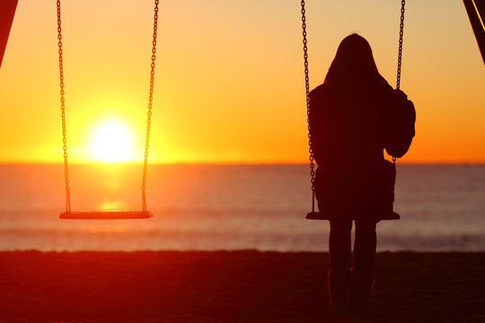 Single woman sitting on a swing contemplating sunset