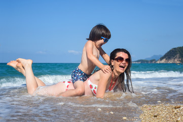 Fototapeta premium Mother and son playing on the beach. Family having fun on beach on travel vacation summer holidays