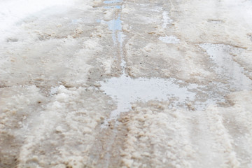 road is paved with cracks in pits and puddles from the snow. Landscape of the winter road in cloudy gray weather.