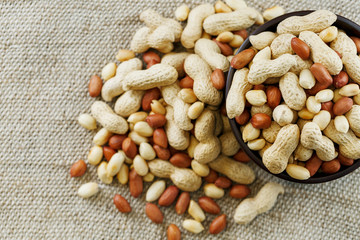 Peanuts in the shell and peeled close-up in cups. Roasted peanuts in their shells and peeled against a brown cloth.
