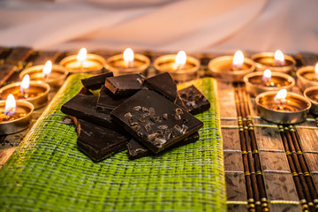 Sweets, milk candies and dark chocolate broken, on the background of lights, candles. Warm, soft and pleasant shade. Dessert is gentle and natural in a romantic home environment.