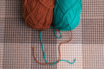 Ball of green and brown knitting yarn. Knitting threads on a background of brown plaid.