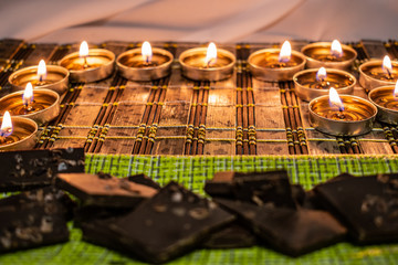 Sweets, milk candies and dark chocolate broken, on the background of lights, candles. Warm, soft and pleasant shade. Dessert is gentle and natural in a romantic home environment.