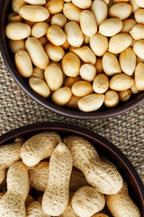 Peanuts in the shell and peeled close-up in cups. Roasted peanuts in their shells and peeled against a brown cloth.