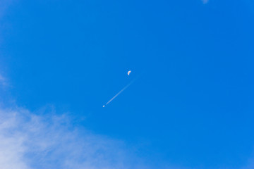 a plane contrail and moon on the bright blue sky