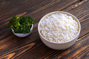 A Cup of white Rice and broccoli on a dark wooden background. Dietary or vegetarian food.