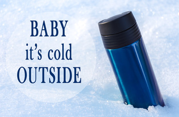 Blue thermo mug in sparkling snow and quote "baby it's cold outside".