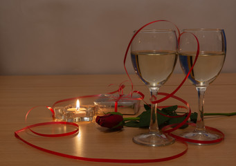 Two glasses with champagne, a candle, a rose and a red ribbon. Meeting