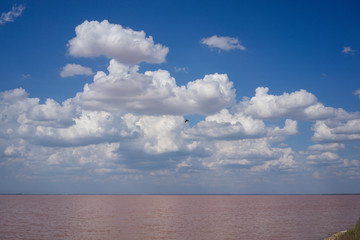landscape overlooking a pink salt lake under a blue sky with clouds