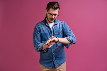 Portrait of a shocked man looking on wrist watch over pink background.