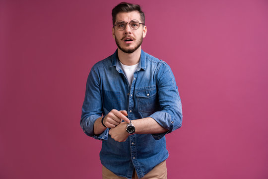 Portrait Of A Shocked Man Looking On Wrist Watch Over Pink Background.