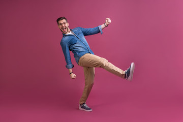Fototapeta na wymiar Funny man in casual is having some fun. He is posing and dancing. Isolated on pink background.