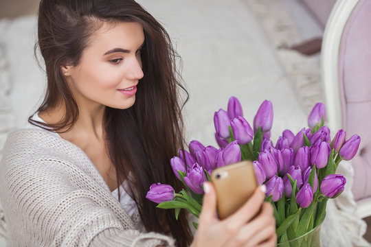 Attractive young woman making selfie indoors. Beautiful female with smartphone making photo. Girl at home portrait.
