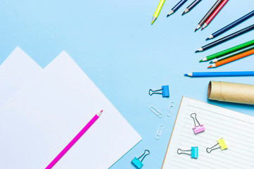 Wooden colored pencils, clean school notebook in line, paper clips on blue background top view flat lay copy space. Pencils for drawing, objects for creativity. Back to school concept.