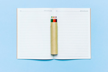 Color pencils and clean notebook in line on blue background top view flat lay copy space. Wooden...