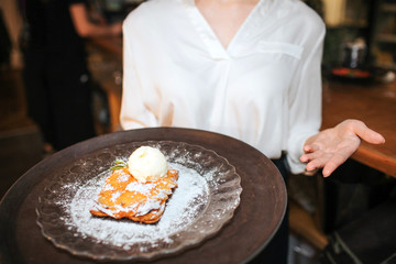 Close up of waitress holding cake on plate on stray. She point on it.