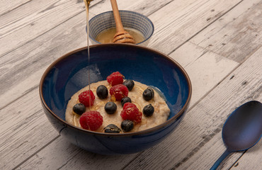 Bowl of porridge with raspberries, blueberries and drizzled honey 