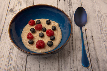 Bowl of porridge with raspberries, blueberries on a wooden background 