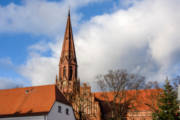 Fototapeta na wymiar Germany, Prignitz, Pritzwalk: Panomaric view of evangelic Sankt Nikolai church in the city center of the German small town with steeple, red roof tops and blue cloudy sky - concept religion Lutheran