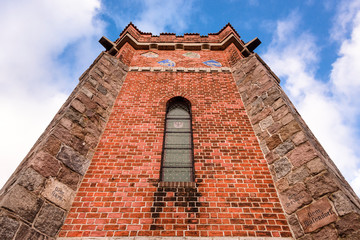 Germany, Pritzwalk, Trappenberg: Historic Bismarck tower (Bismarckturm) from below with red brick exterior wall, window, crests, battlements, observation deck and blue cloudy sky - concept monument
